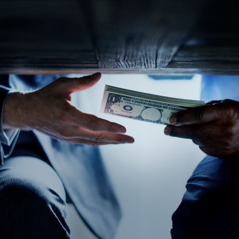 A discreet cash handover under a table, showing how bribery can happen quietly.